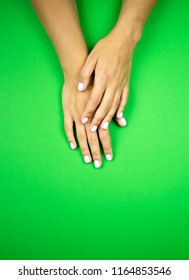 A young beautiful girl showing her tender hands with nice white or pastel pink manicured nails on a green background in a beauty salon. Flat lay photo. - Shutterstock ID 1164853546