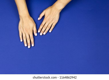 A young beautiful girl showing her tender hands with nice white or pastel pink manicured nails on a blue background in a beauty salon. Flat lay photo.
