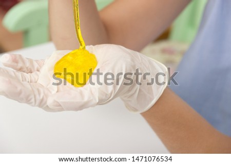 Young beautiful girl shows how to make slime. Yellow homemade slime is a children's toy. Composition sodium tetraborate and glue. hands in medical gloves and a yellow liquid.