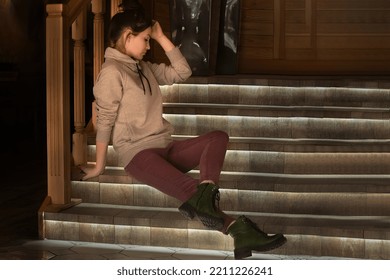 A Young Beautiful Girl Sits Alone On The Stairs Indoors And Thinks About Something