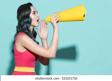 Young beautiful girl speaks in a paper loudspeaker on a blue background.