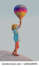 Young Beautiful Girl In Straw Hat Is Trying To Catch The Hot Air Baloon - Cappadocia, Turkey