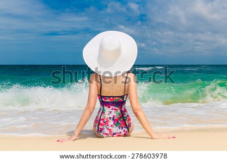 Young beautiful girl in a straw white hat back to the viewer on the beach of a tropical island. Summer vacation concept.