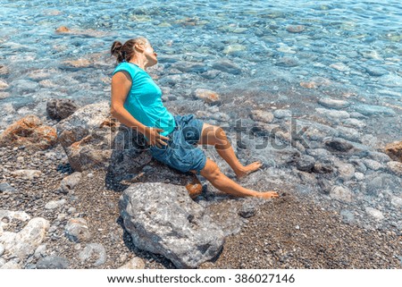 Young beautiful girl in trendy hairstyle playing by the sea in a beautiful beach in Santorini, Greece.