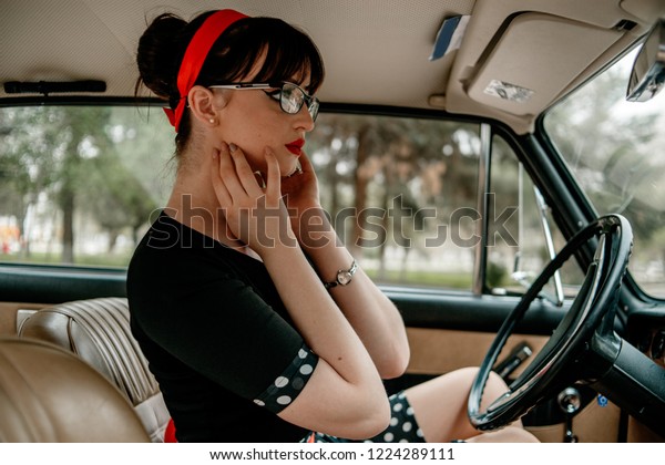 Young beautiful girl in vintage\
clothes sitting and posing in a retro car. Without\
retouching.