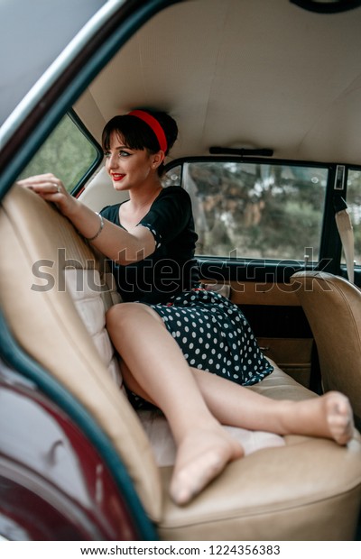 Young beautiful\
girl in vintage clothes sitting and posing in the back seat of a\
retro car. without\
retouching