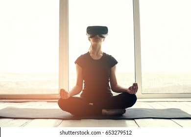 A young beautiful girl in virtual reality glasses makes yoga and aerobics remotely. Future technology concept. Modern imaging technology. Classes in single sports remotely. - Powered by Shutterstock