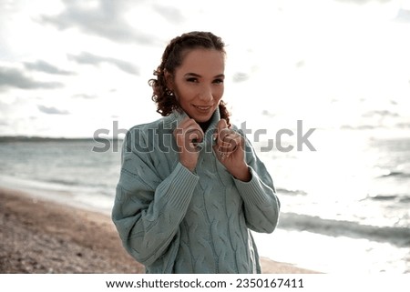 Young beautiful girl walking in the sand beach in cold weather day. Woman dressed warm clothes. 