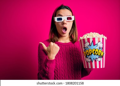 Young beautiful girl watching movie using 3d glasses eating box with popcorns Surprised pointing with hand finger to the side, open mouth amazed expression.