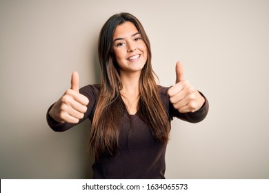 Young beautiful girl wearing casual sweater standing over isolated white background approving doing positive gesture with hand, thumbs up smiling and happy for success. Winner gesture.