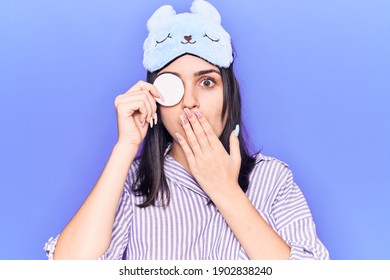 Young Beautiful Girl Wearing Funny Sleep Mask Using Makeup Remover Cotton Covering Mouth With Hand, Shocked And Afraid For Mistake. Surprised Expression 