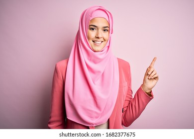 Young Beautiful Girl Wearing Muslim Hijab Standing Over Isolated Pink Background With A Big Smile On Face, Pointing With Hand Finger To The Side Looking At The Camera.