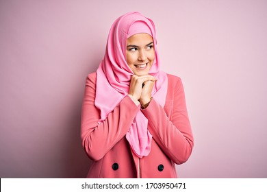 Young Beautiful Girl Wearing Muslim Hijab Standing Over Isolated Pink Background Laughing Nervous And Excited With Hands On Chin Looking To The Side