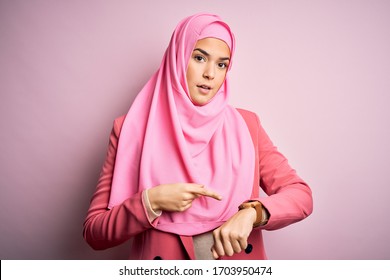 Young beautiful girl wearing muslim hijab standing over isolated pink background In hurry pointing to watch time, impatience, upset and angry for deadline delay