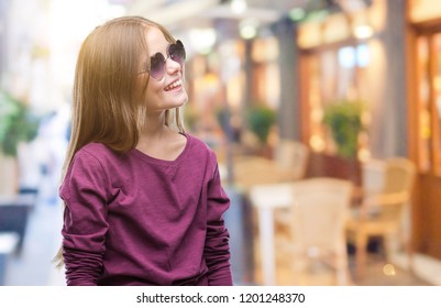 Junge schöne Mädchen mit Sonnenbrille auf isoliertem Hintergrund, die mit einem Lächeln auf Gesicht, natürlichem Ausdruck zur Seite schaut. Lachen selbstbewusst.