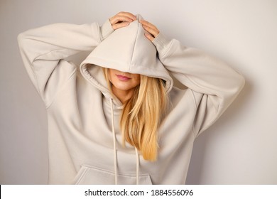 Young Beautiful Girl In A White Hoodie Posing. Warm Oversized Hoodie With An Hood. Stylish Trendy Hipster Bow. Trying On Clothes In A Store. Youth Subculture. Fashion Clothing Advertising