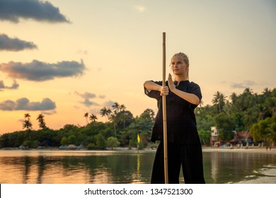 Young Beautiful Girl Woman Blond Doing Kung Fu With Bamboo Stick On The Seashore At Sunset