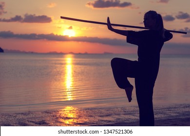 Young Beautiful Girl Woman Blond Doing Kung Fu With Bamboo Stick On The Seashore At Sunset