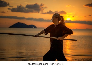 Young Beautiful Girl Woman Blond Doing Kung Fu With Bamboo Stick On The Seashore At Sunset