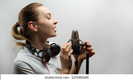 Young beautiful girl writes vocals, radio, voiceover tv, reads poetry, blog, podcast in studio on studio microphone in headphones on white background