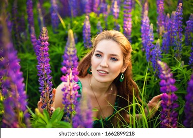 A young beautiful girl in a yellow dress holds a large bouquet of purple lupins in a blooming field. Blooming Lupin flowers. environmentally friendly. The concept of nature. Soft focus.