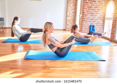 Young beautiful group of sportswomen smiling happy practicing yoga. Sitting doing boat pose at gym