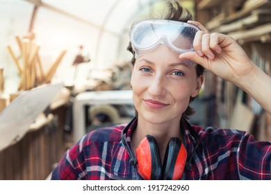 Young Beautiful Handy Professional Happy Female Strong Carpenter Portrait Wearing Protective Goggles Working In Carpentry Diy Workshop Against Wood. Confident Engineer. Women Male Hobby At Workbench