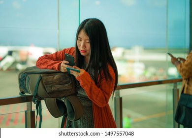 Young Beautiful And Happy Asian Chinese Woman Checking Mobile Phone Holding Passport In Her Hand At Airport Departure Lounge Carrying Backpack Waiting For Boarding Ready For Holiday