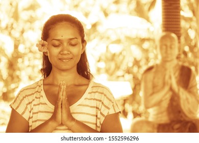 young beautiful and happy Asian Indonesian woman with Balinese style ear flower in Namaste hands pose smiling at yoga studio relaxed and zen like in harmony in sepia color grade