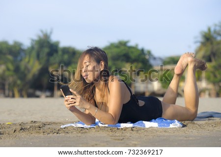 young beautiful and happy Asian woman using mobile phone texting on internet social media smiling relaxed lying on beach sand having suntan enjoying tropical holiday and vacation