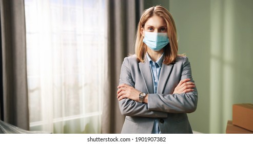 Young Beautiful Happy Caucasian Woman Real Estate Agency Manager In Mask Standing In Empty House And Looking At Camera. Realtor Concept. Selling Property Business. 