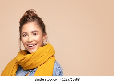 Young beautiful happy girl posing in studio wearing fashionable scarf and jeans jacket. Smiling woman looking at camera. Human emotions,, expression. Beige studio background.