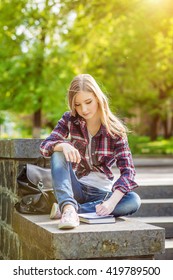 Young beautiful happy girl student sitting on the steps under the campus, university, school, education preparing to passing exam read the synopsis of the book in a notebook. Emotion