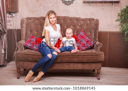 Young beautiful happy mother with a young child sitting on the couch and looking at the camera. Mother's day. Happy mother with her son.