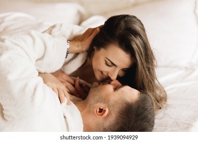 Young beautiful happy newlyweds in love a man and a woman lie in bed, smile and hug in the house