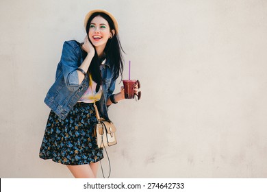 Young Beautiful Happy Stylish Hipster Girl, Cocktail, Smoozy Drink, Denim Jacket, Smiling, Fashion, Teen, Cool Accessories, Purse, Hat, Sunglasses, Amazed, Vintage Style, Wall Background, Hair, Wind