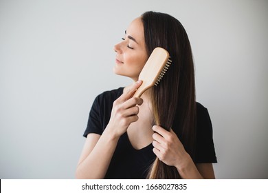 Joven mujer feliz cepilla su largo y saludable cabello con un cepillo de madera sobre fondo blanco. Colocar texto.