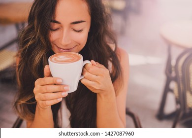 Young beautiful happy woman with long curly hair enjoying cappuccino in a street cafe - Powered by Shutterstock