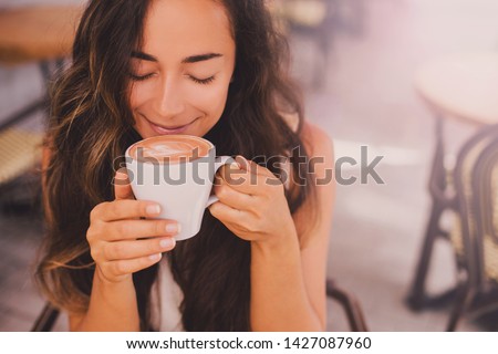 Young beautiful happy woman with long curly hair enjoying cappuccino in a street cafe