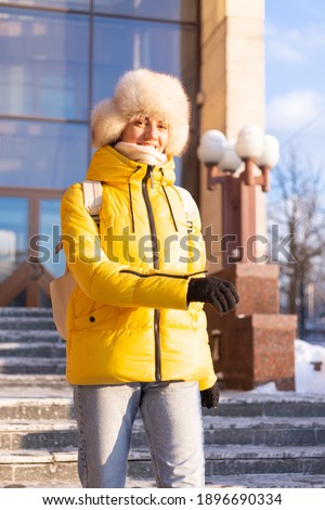 Young beautiful happy woman outdoors on a sunny day in warm clothes and a winter Russian siberian hat backpack travel around city