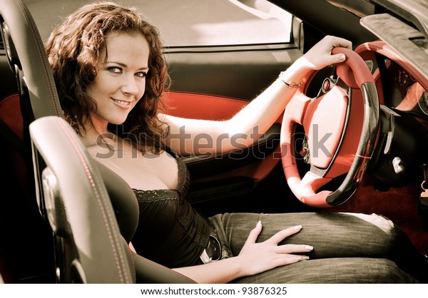 Young beautiful happy woman in sport car\
holding steering wheel - red interior\
detail
