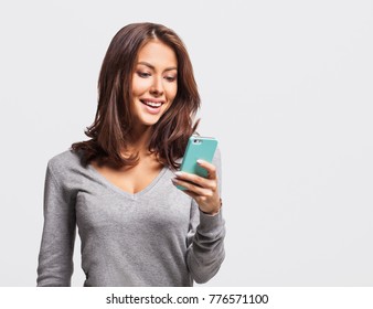 Young beautiful happy woman using smart phone. Excited surprised girl texting on her mobile phone. Studio shot isolated on grey background. Technology, connection, communication, social media concept