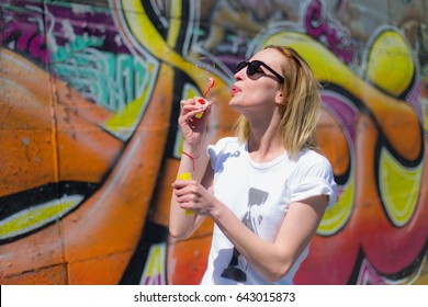 Young beautiful hipster woman bubble blower in the city. Background graffiti. Summer in the city. Blonde in the background of graffiti - Powered by Shutterstock