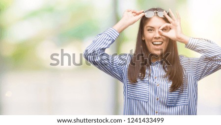 Young beautiful hispanic business woman doing ok gesture with hand smiling, eye looking through fingers with happy face.