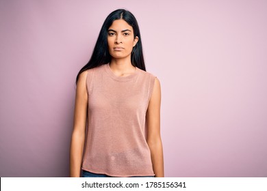 Young Beautiful Hispanic Fashion Woman Wearing Casual Sweater Over Pink Background With Serious Expression On Face. Simple And Natural Looking At The Camera.