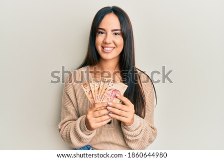 Young beautiful hispanic girl holding mexican pesos smiling with a happy and cool smile on face. showing teeth. 
