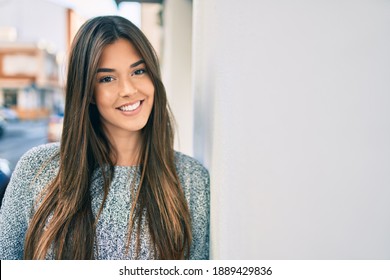 Young beautiful hispanic girl smiling happy leaning on the wall at the city.
