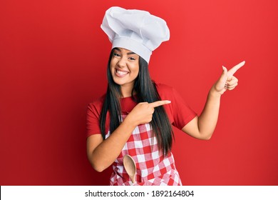 Young beautiful hispanic girl wearing baker uniform and cook hat smiling and looking at the camera pointing with two hands and fingers to the side.  - Powered by Shutterstock