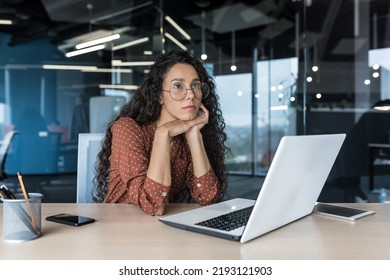 Young Beautiful Hispanic Woman With Curly Hair And Glasses, Working In Modern Office Using Laptop, Female Worker Thinking And Sad, Business Woman Upset