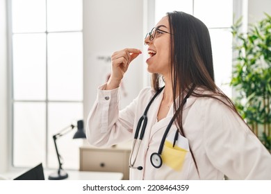 Young Beautiful Hispanic Woman Doctor Smiling Confident Taking Pill At Clinic